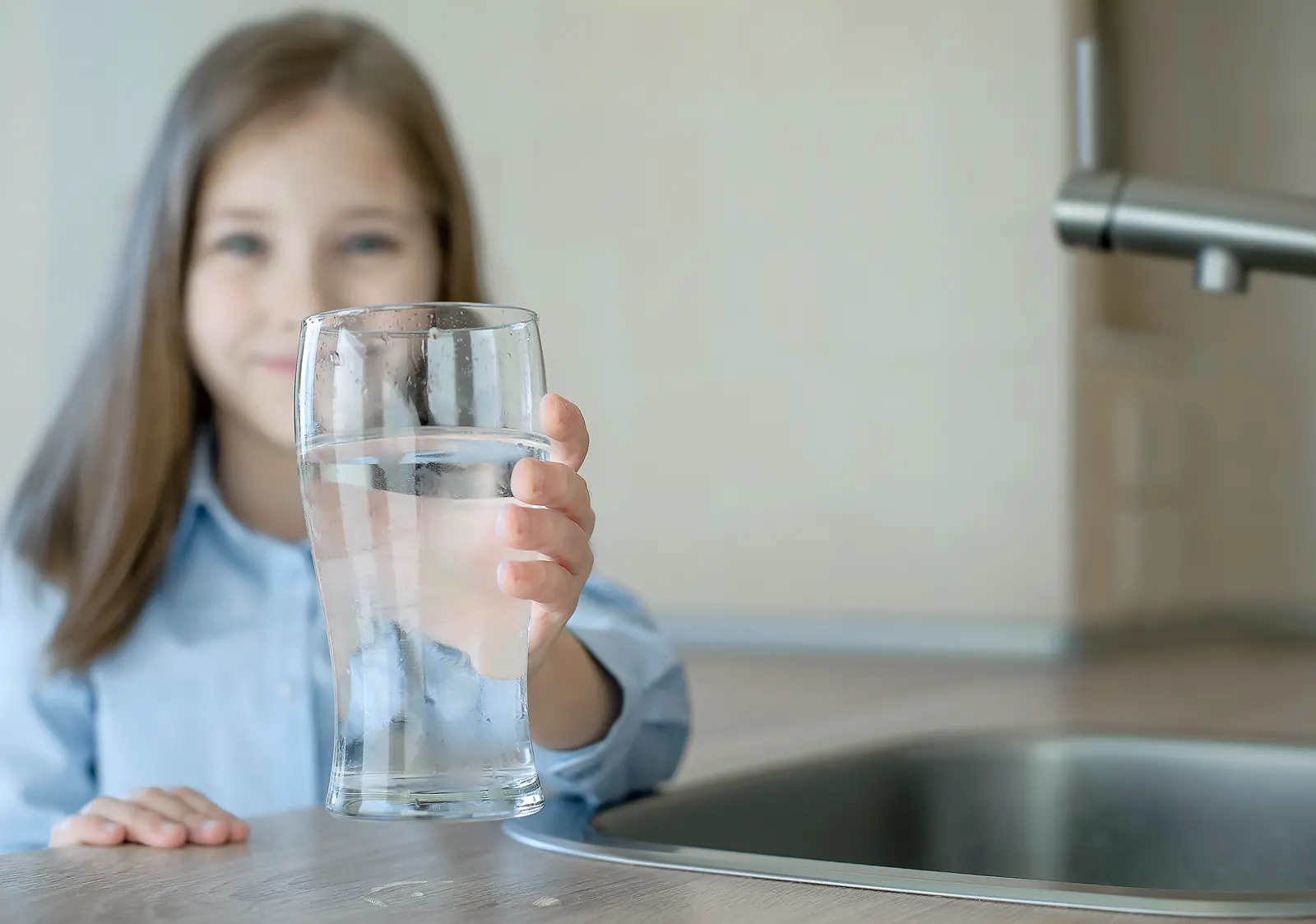 Girl holding a tall glass of water at a kitchen sink